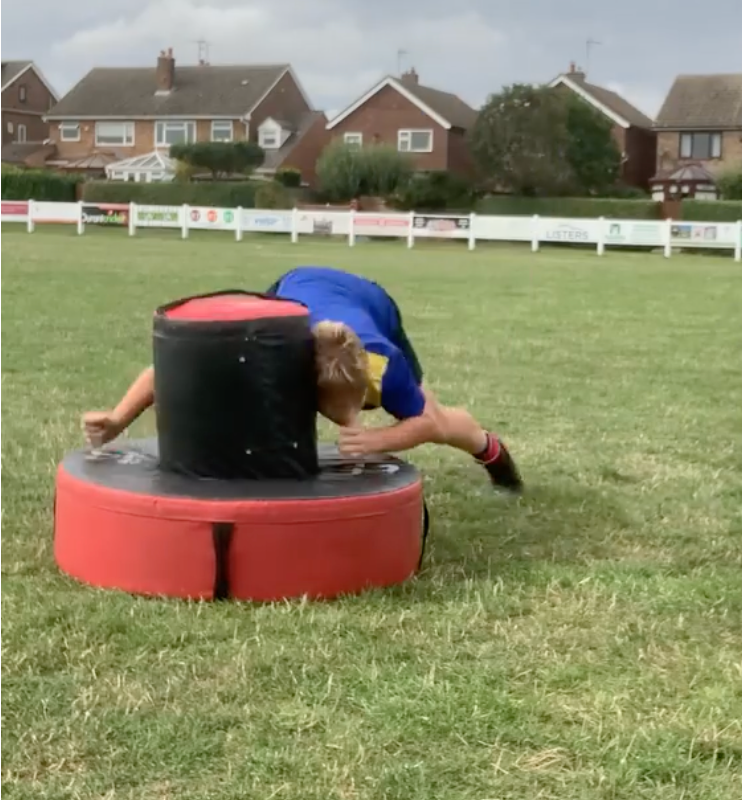 Ram Rugby Rip-Roller Tackle Bag in blue nylon with straps held by player during rugby training drill outdoors on grass field